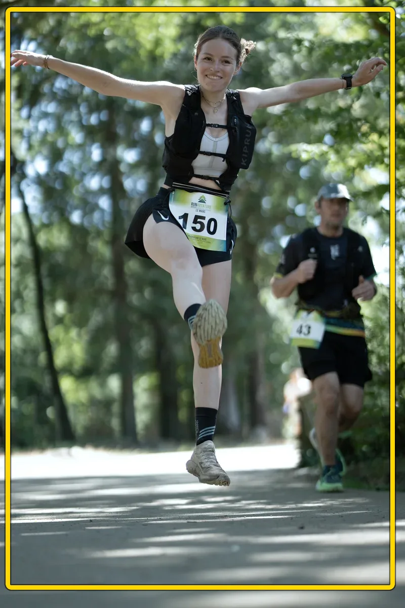 Runner with bib 150, mid-jump — plein cadre brut, penché avant redressement
